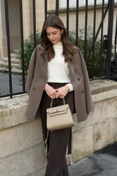 a lady in a white sweater, a brown wool jacket and a pair of grey pants